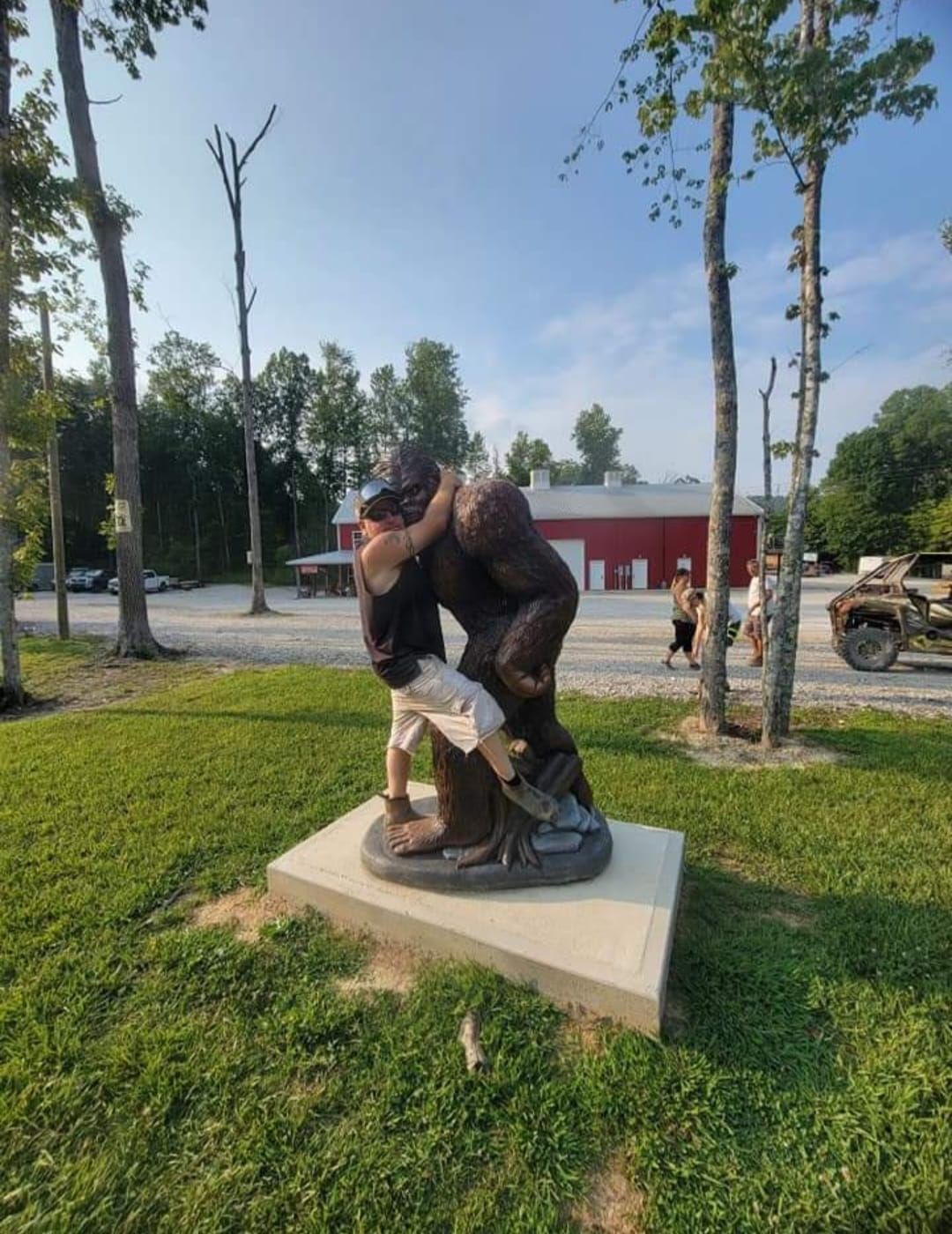 Statue of a man wrestling a large Bigfoot-like creature. Green grass, trees, and red building in the background.