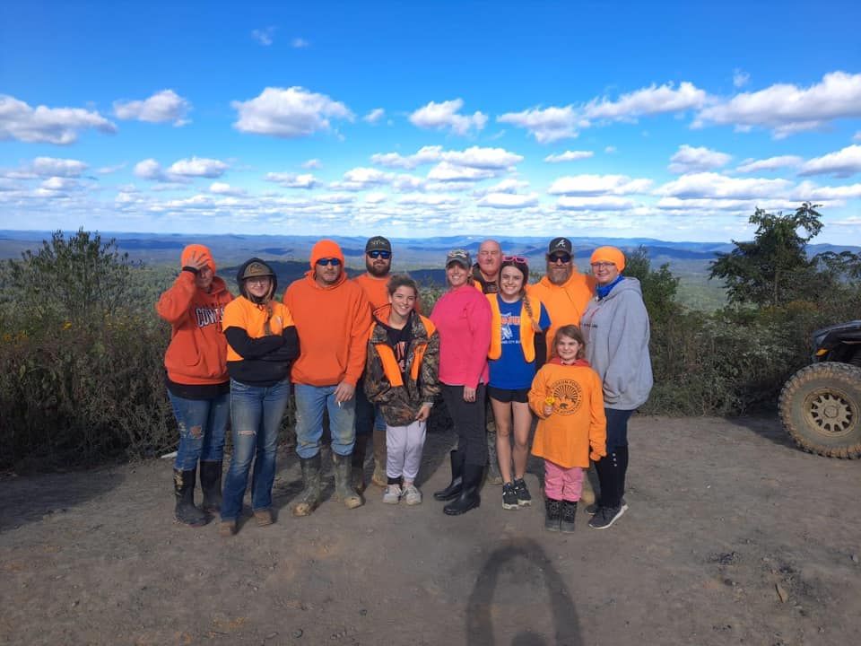 Group of people wearing orange clothing stands on a hilltop with a blue sky background.