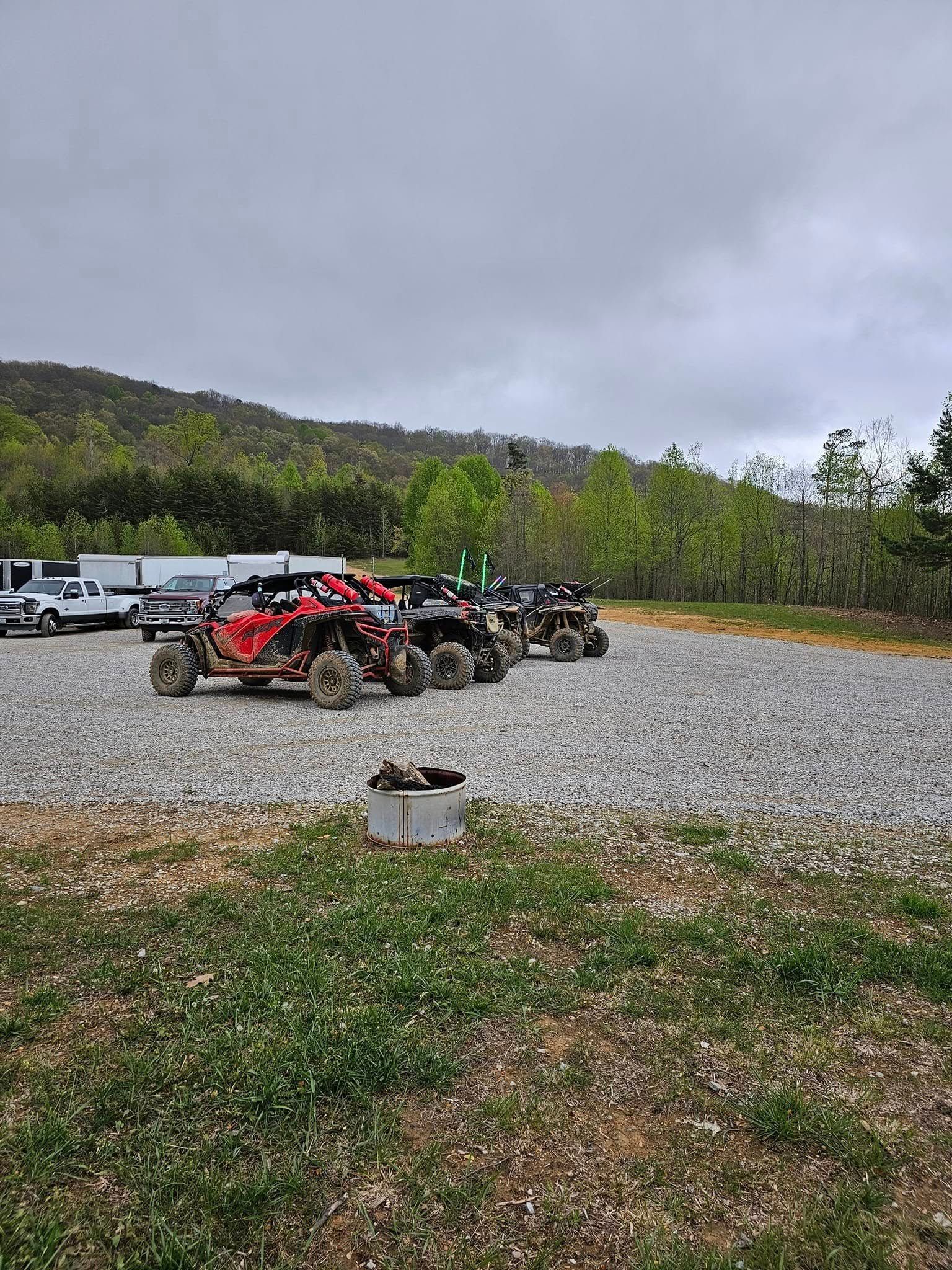 ATVs parked on gravel in a rural area with overcast skies and a mountain in the background.