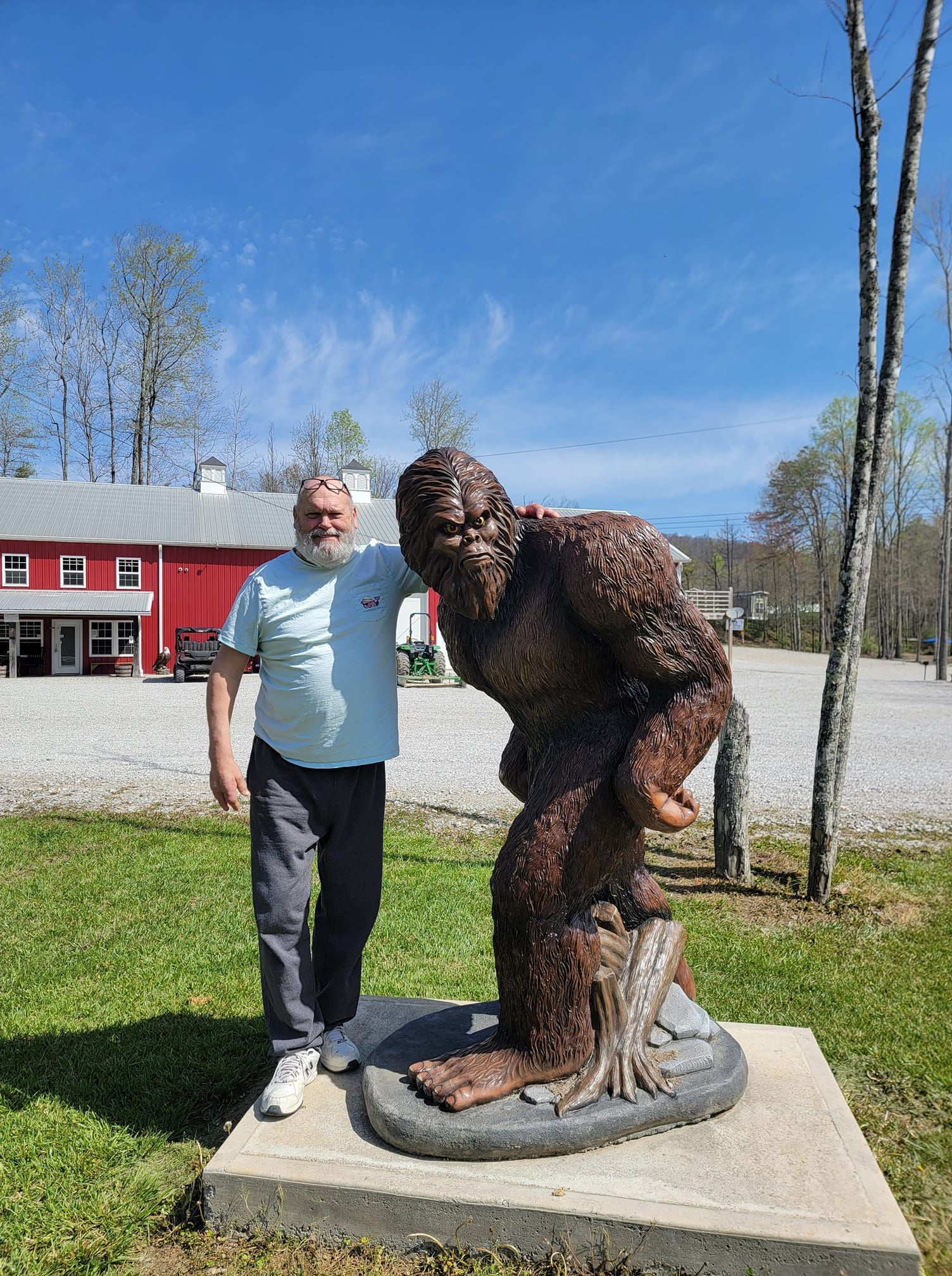 Man poses next to Bigfoot statue in front of a red building and blue sky.