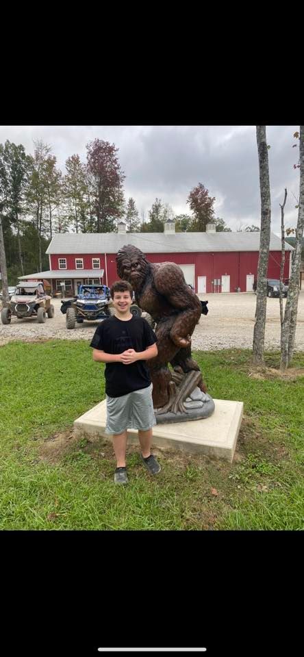 A person stands next to a Bigfoot statue in front of a red building.