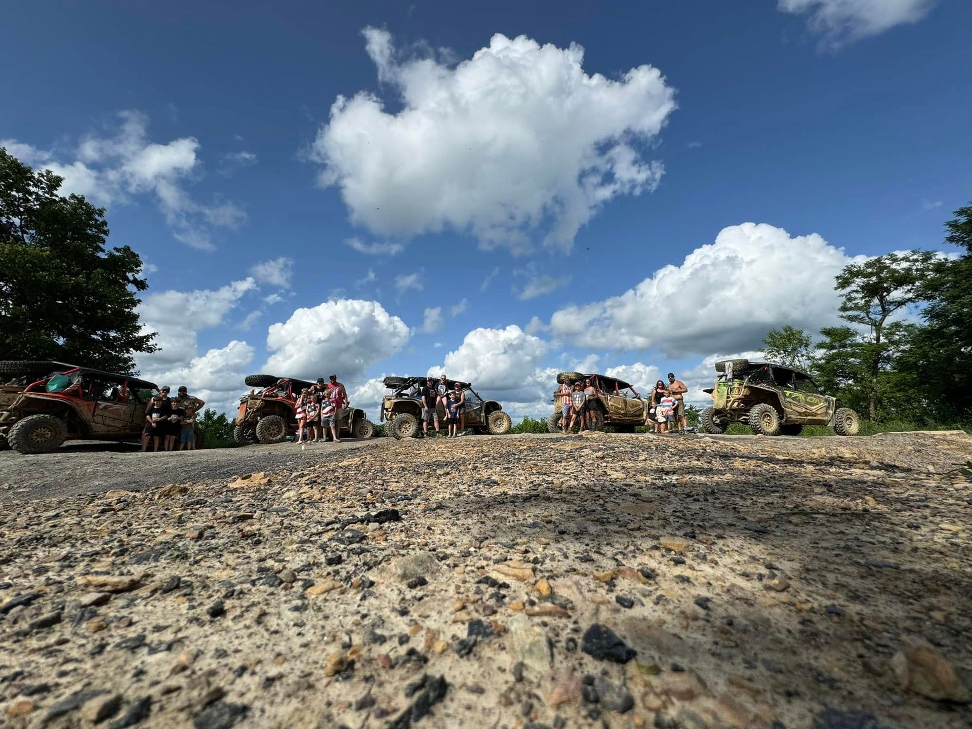 Off-road vehicles with people on a gravel road under a blue sky with fluffy clouds.