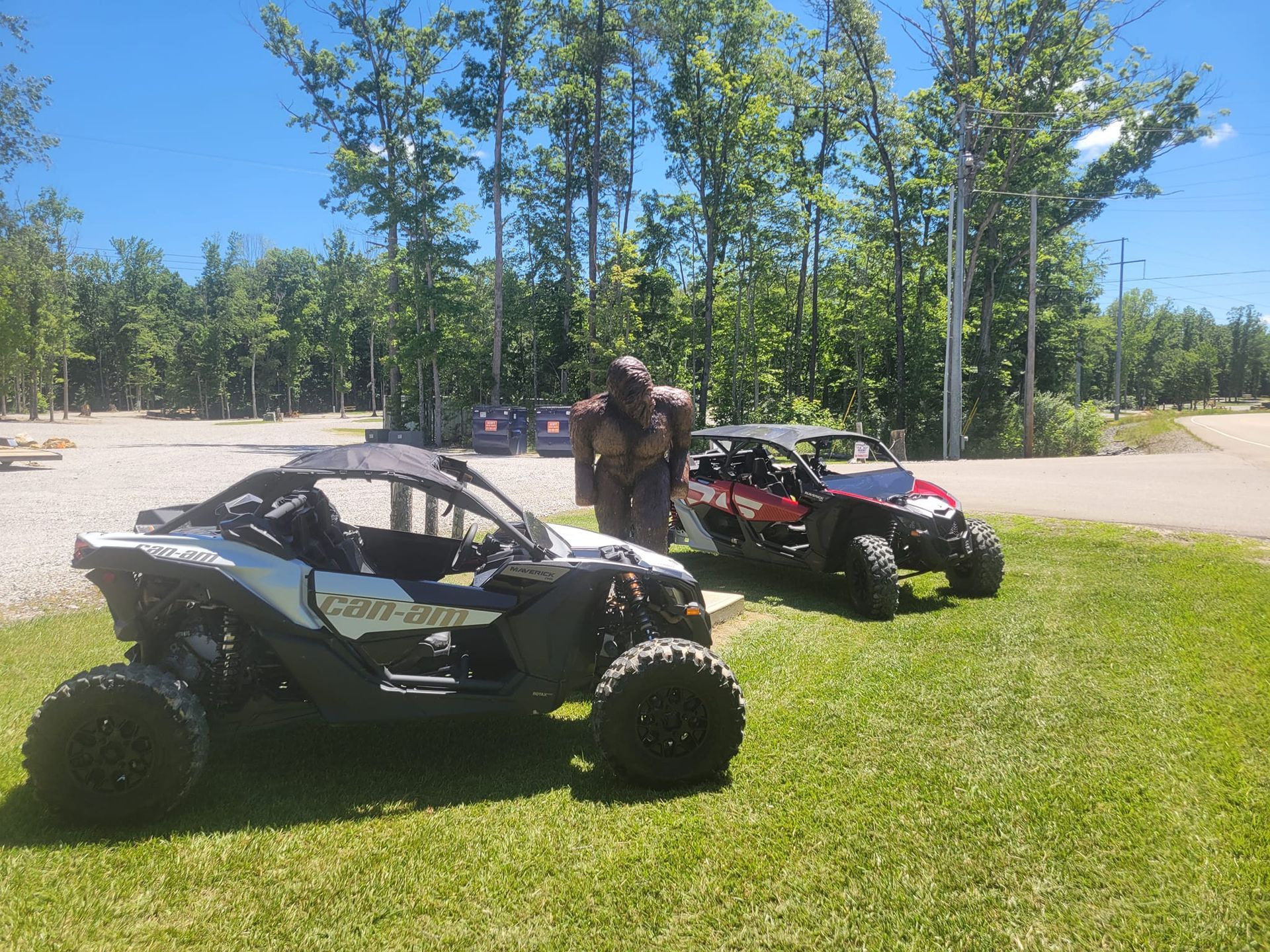 Two Can-Am off-road vehicles on grass, parked near a statue on a sunny day.