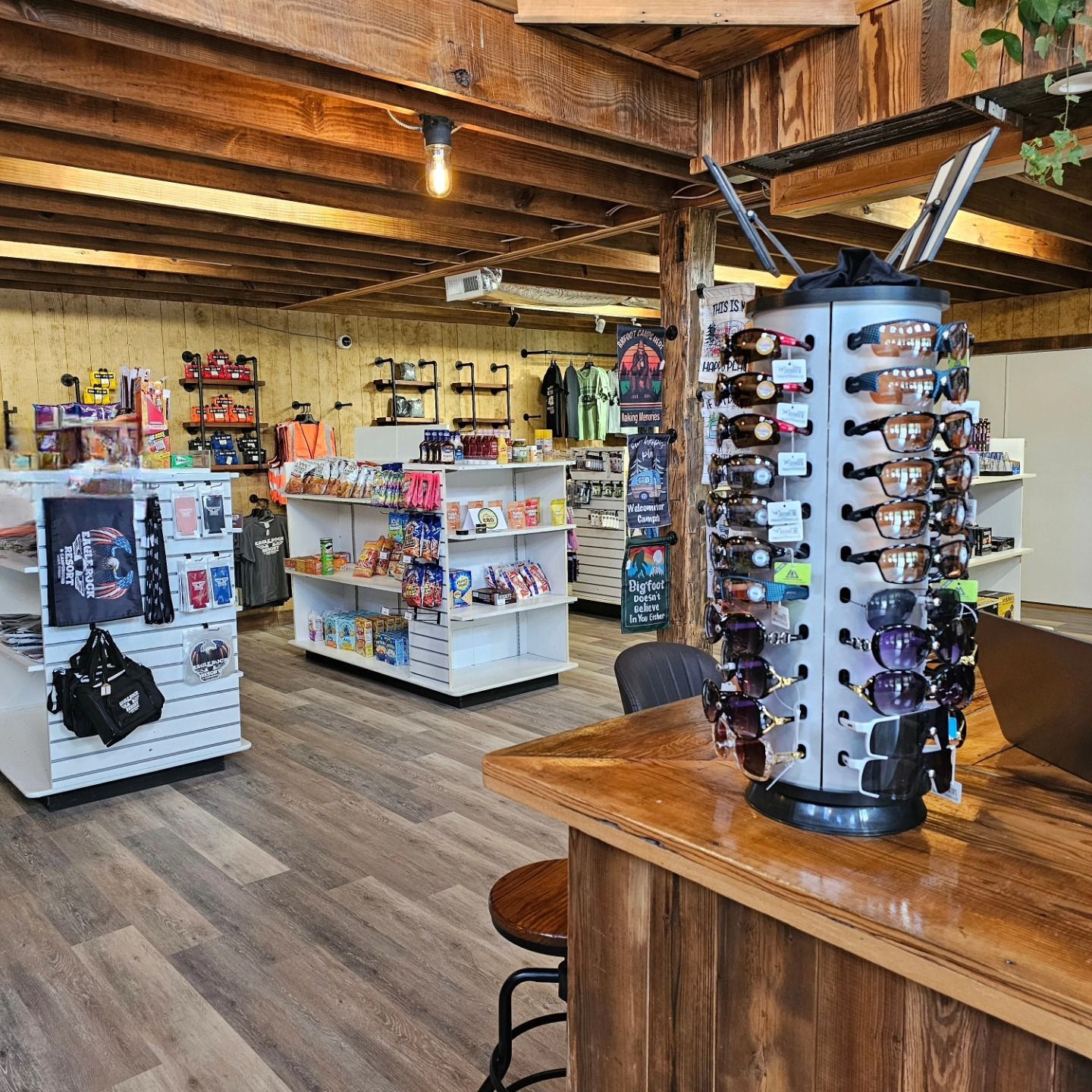 Interior shot of a gift shop with sunglasses display on counter and merchandise on shelves; wooden beams and floors.