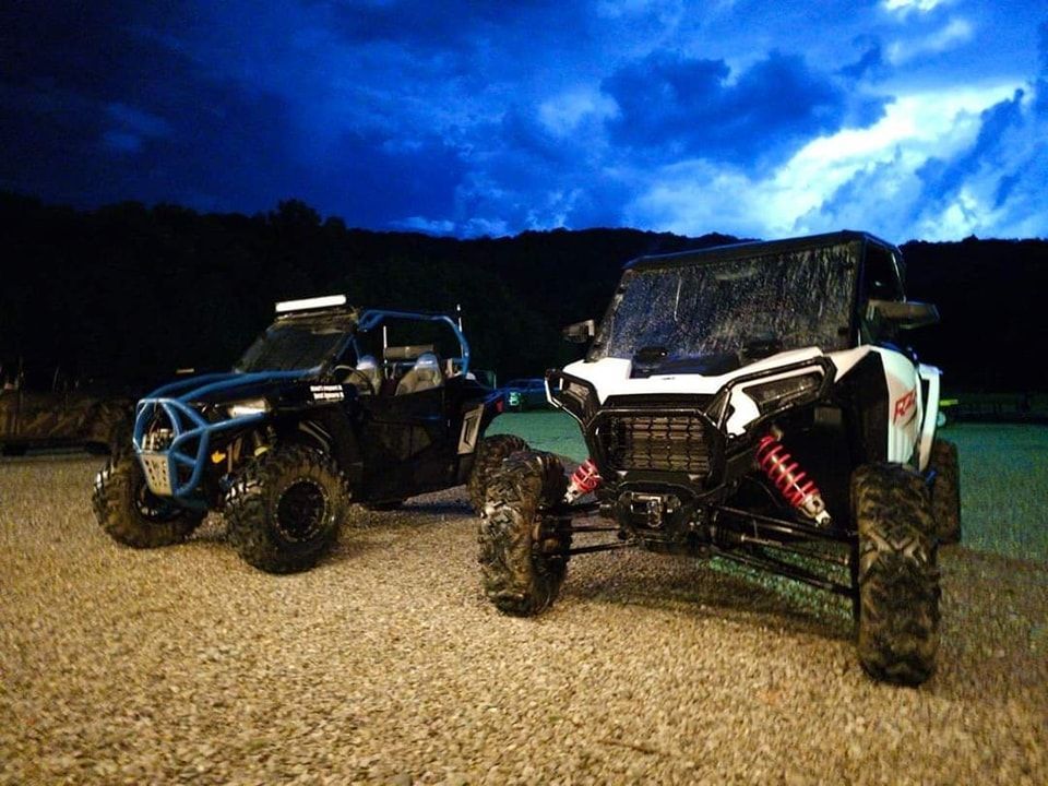 Two off-road vehicles parked on a gravel surface at dusk; one black, one white.