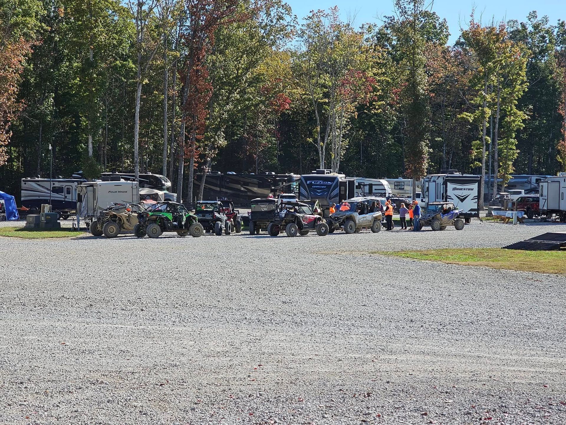 Campground scene: RVs and ATVs parked on gravel; trees in background.