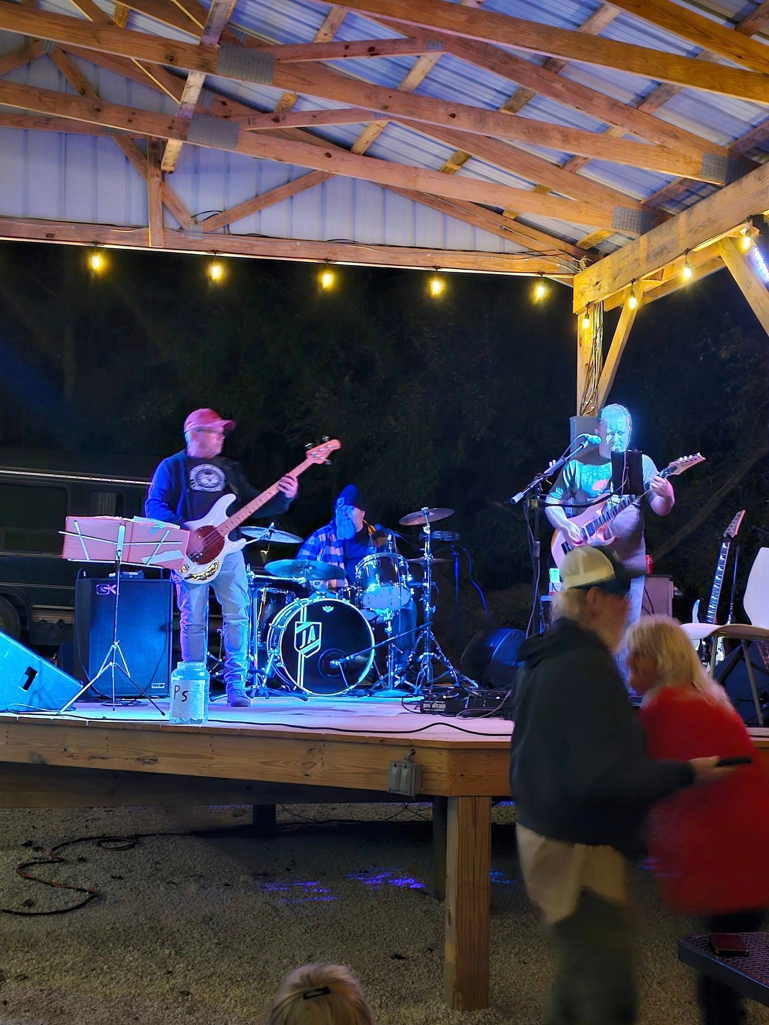 A band performs on an outdoor stage at night. Blue stage lights, people in the audience.