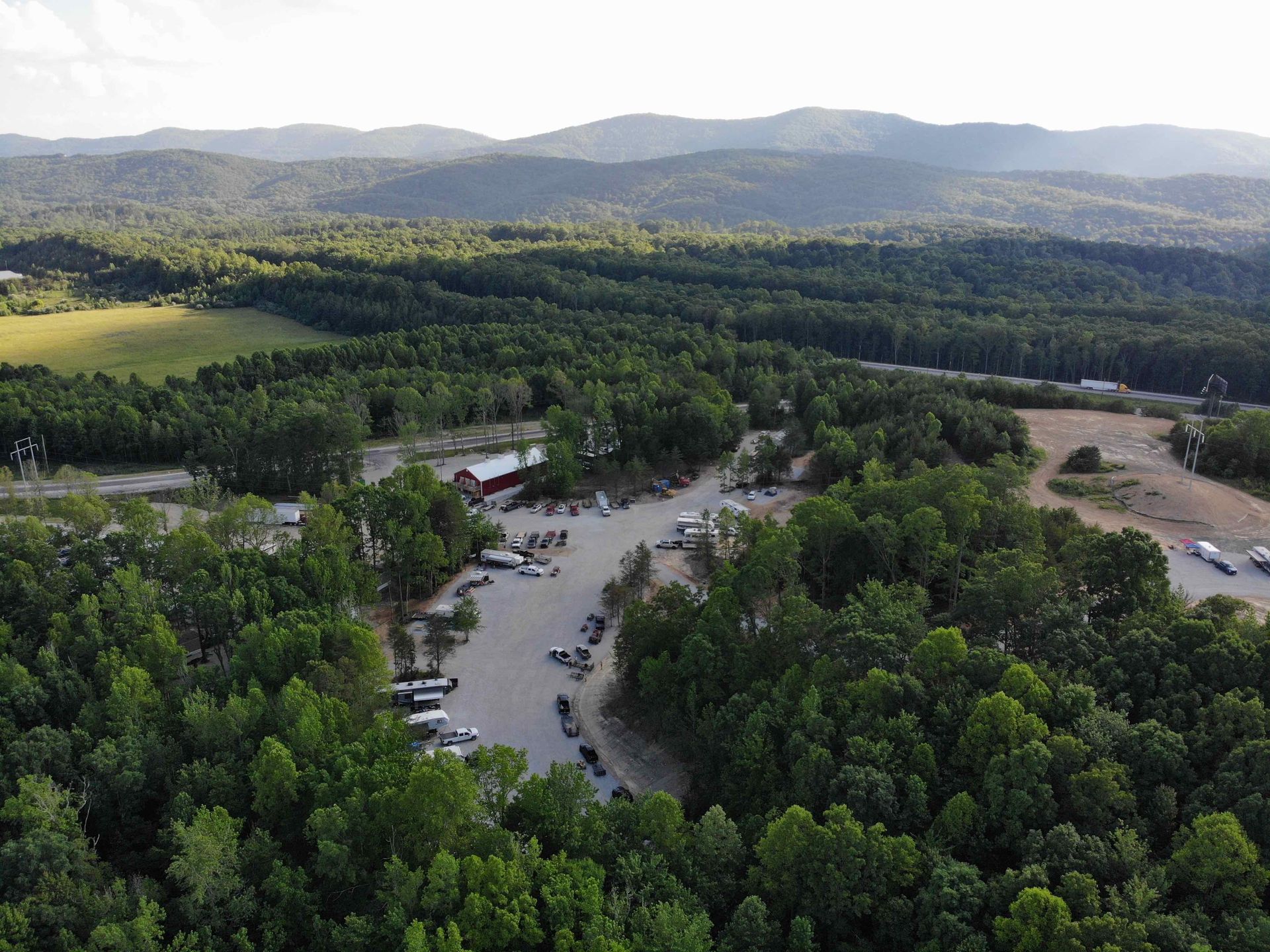 Aerial view of a parking lot surrounded by green trees, with a barn and mountains in the background.
