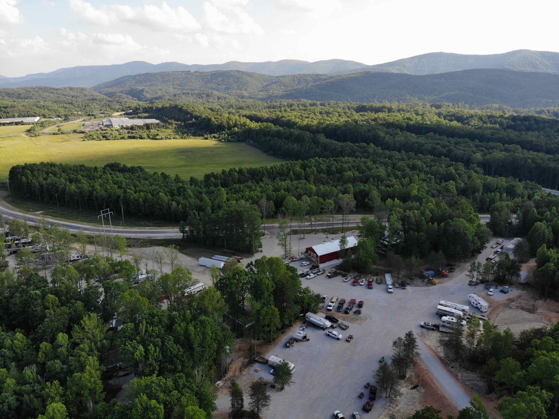 Aerial view of a parking area, red building, field, and trees with mountains in the background.