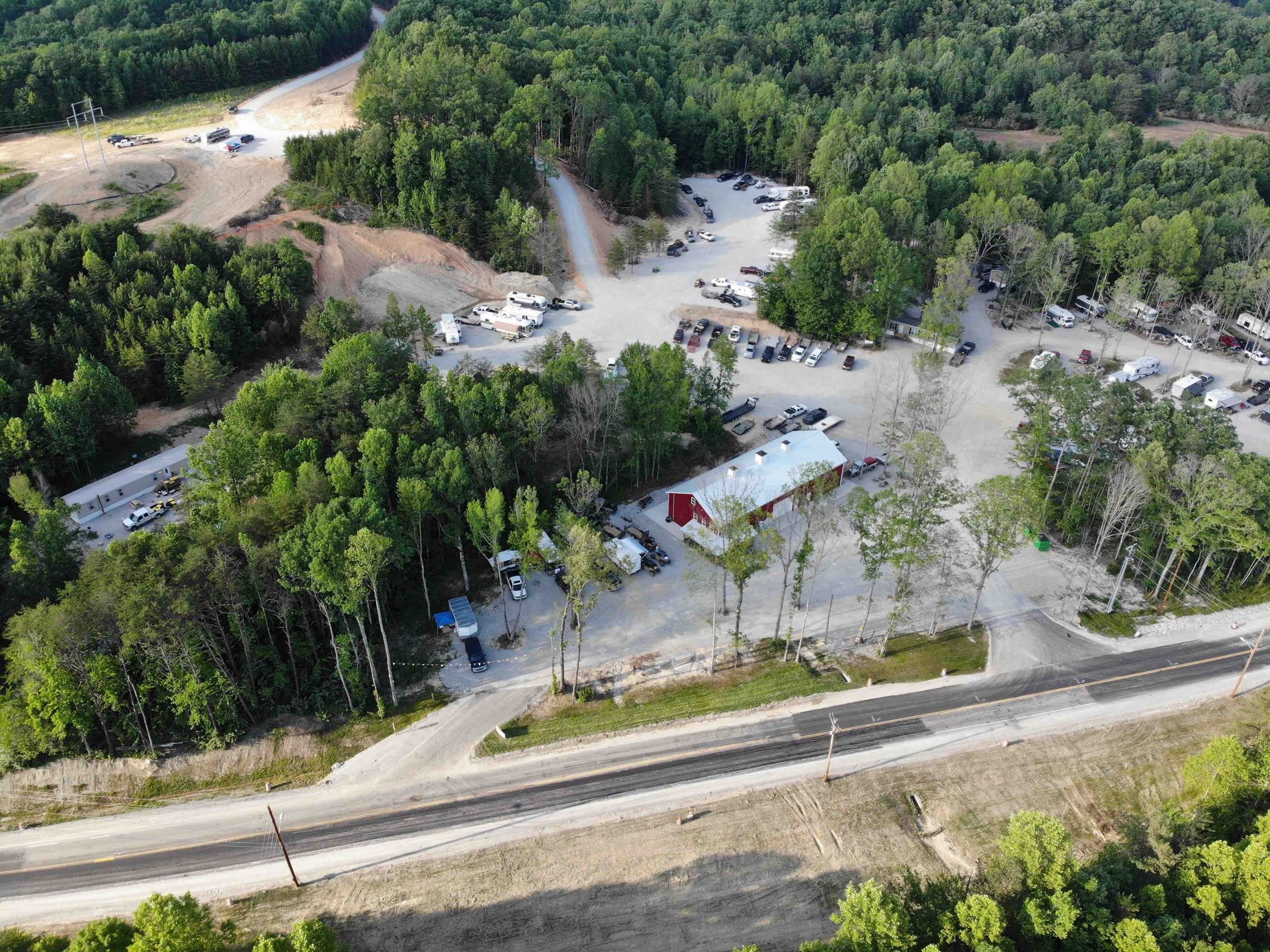 Aerial view of a business with a red roof, surrounded by trees and a parking area near a road.