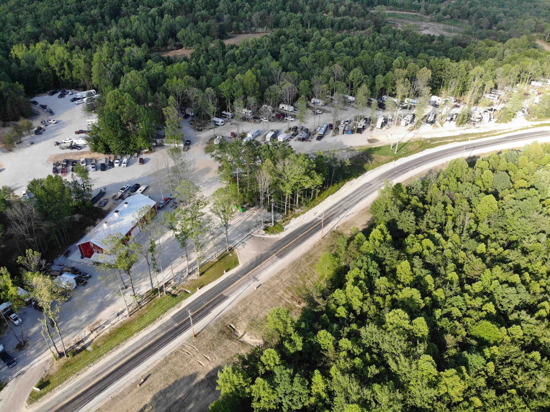 Aerial view of a road cutting through a wooded area, with parking and buildings visible.