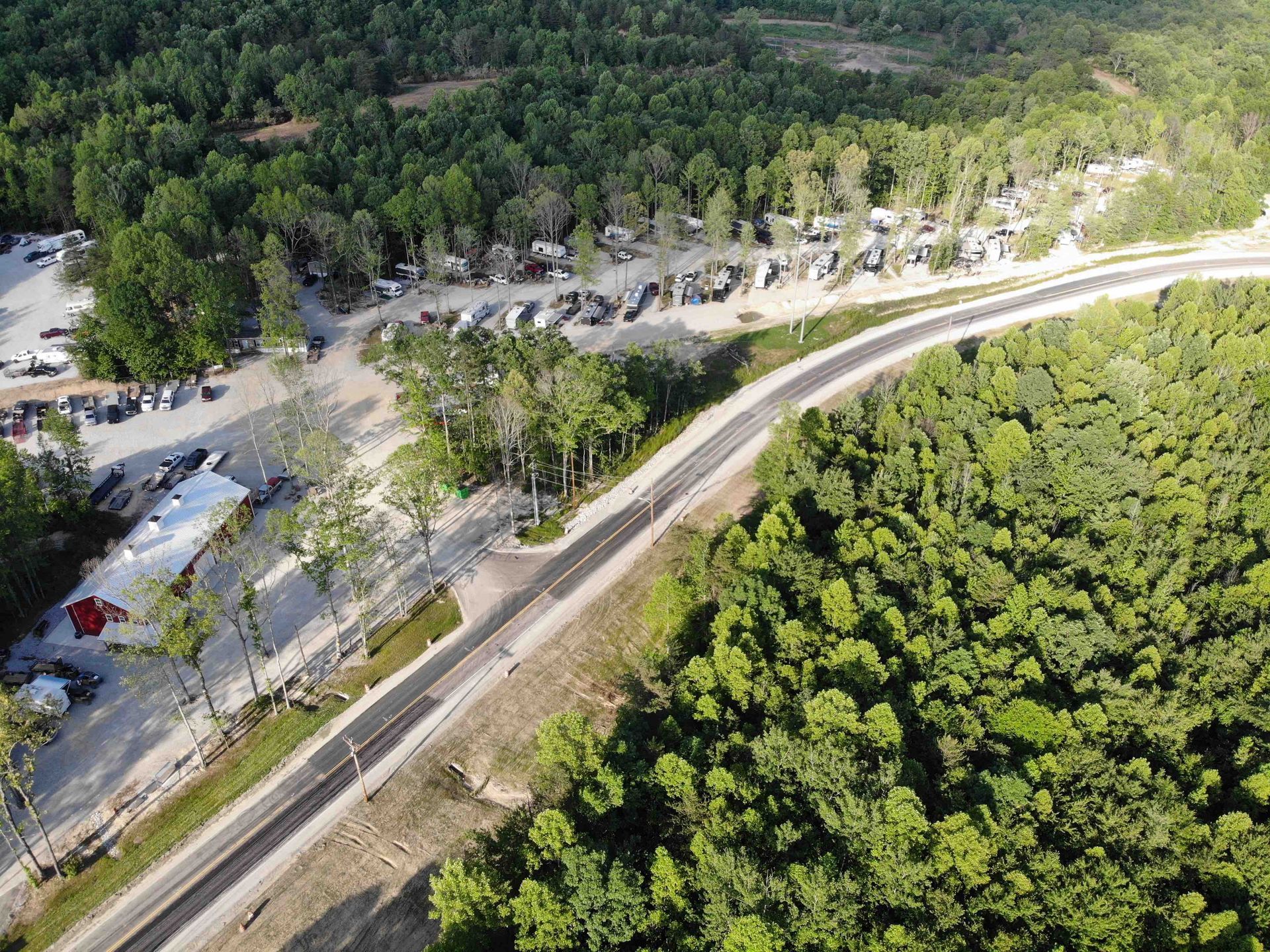 Aerial view of a road cutting through a forest. Cars parked on one side. Trees dominate the landscape.
