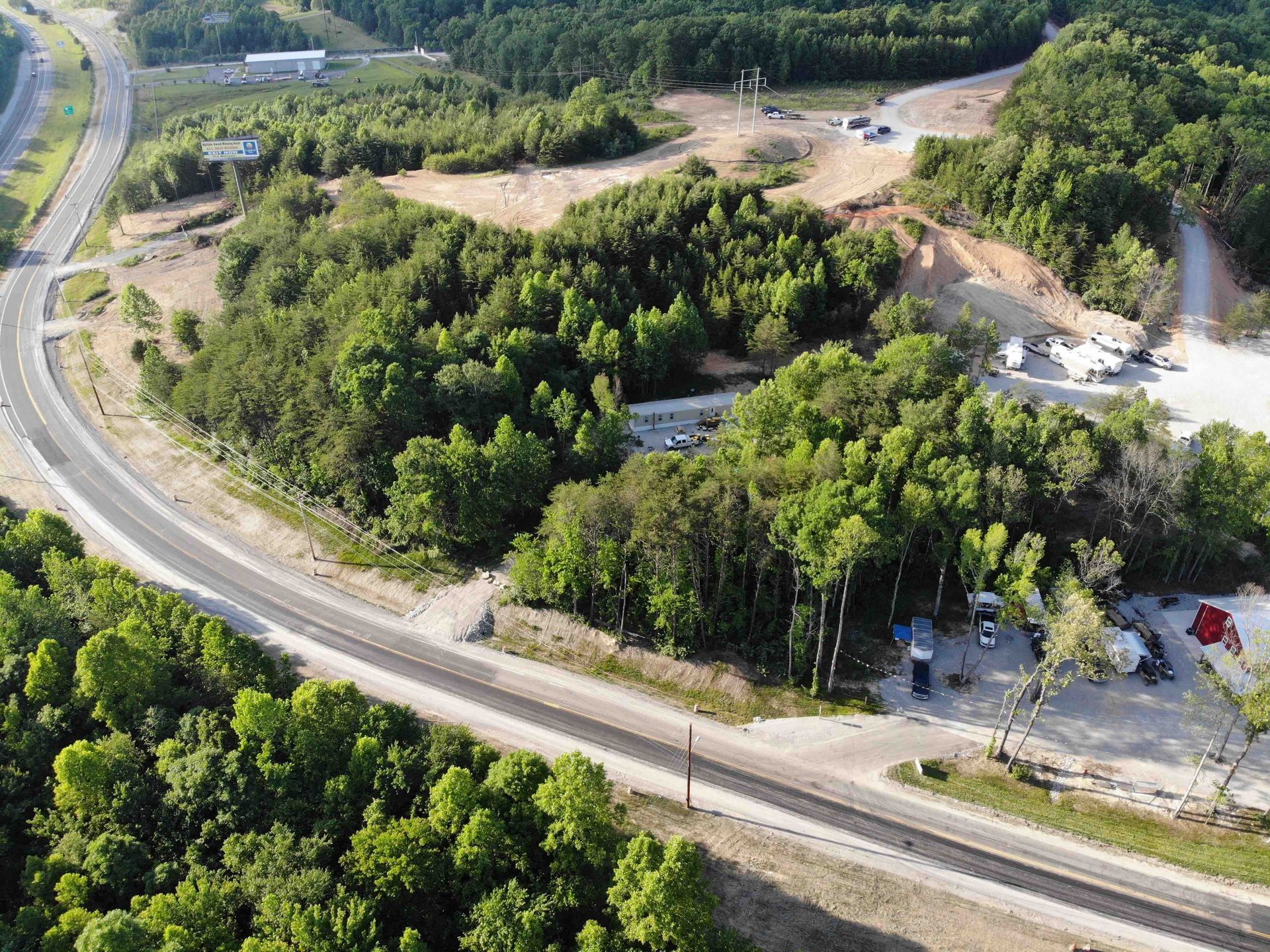 Aerial view of a road winding through a forested area, with signs of construction.