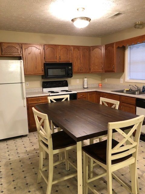 Kitchen with brown cabinets, white appliances, a dark-topped table, and four cream-colored chairs.