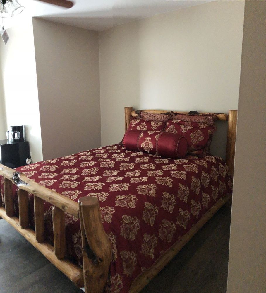 Wooden-framed bed with burgundy floral bedding in a corner nook, against beige walls.