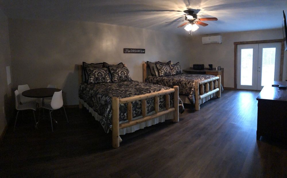A room with two log-style beds, a small table with chairs, and a door leading outside.
