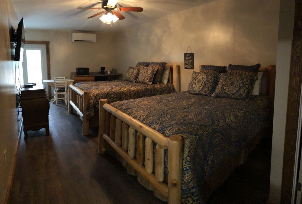 Two double beds in a motel room with dark wood furniture, a TV, and a door to the outside.