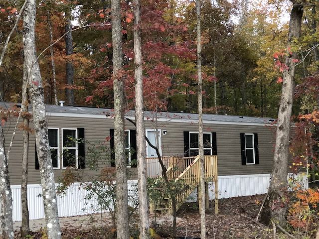 Mobile home nestled in woods with fall foliage. Brown siding, white trim, and black shutters.