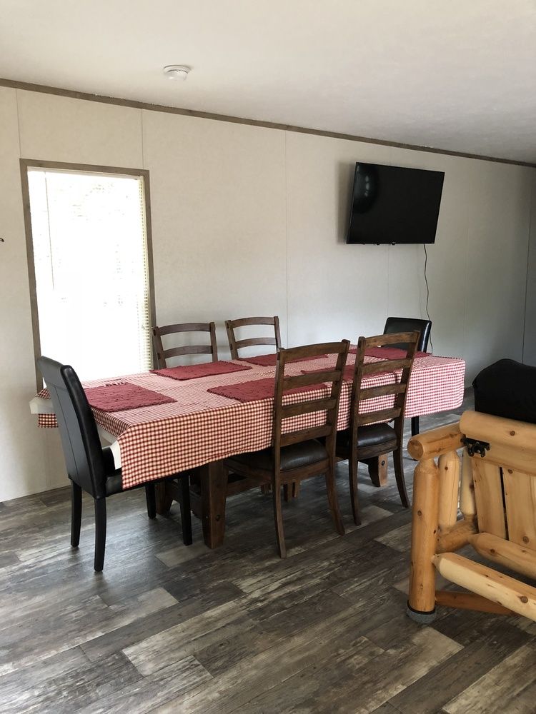 Dining area with table, chairs, TV on wall, and wooden furniture. White walls, wood-look flooring.