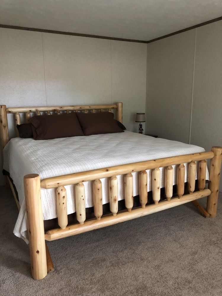 Log cabin style bed with light wood frame, white bedding, brown pillows, and a small lamp.