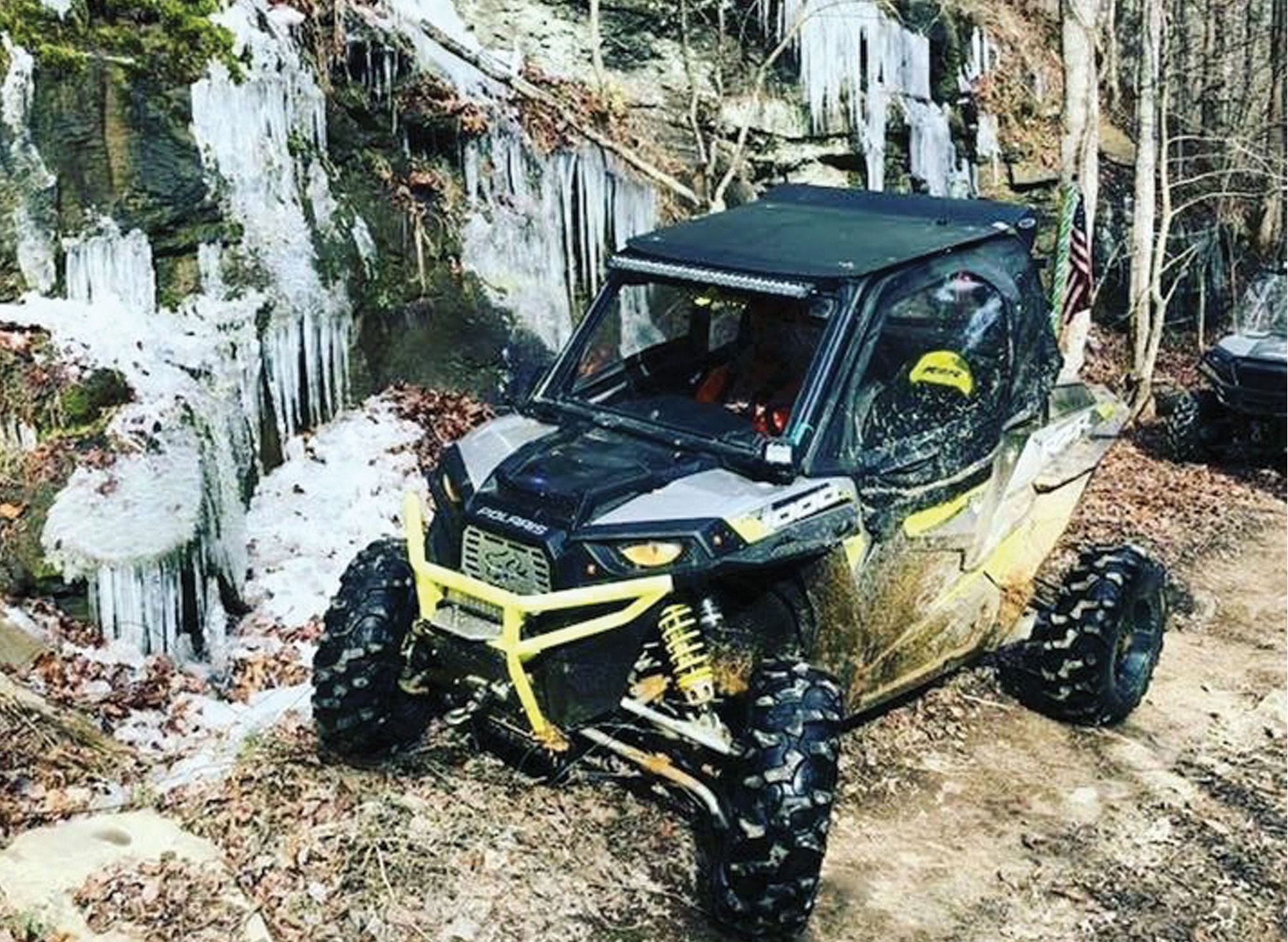 Yellow and black ATV with a roof, parked on a dirt path with icicles in the background.