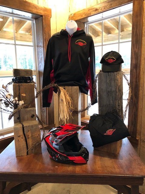 Display of motorcycle gear, including a hoodie, hat, helmet, and bag, on a wooden table.