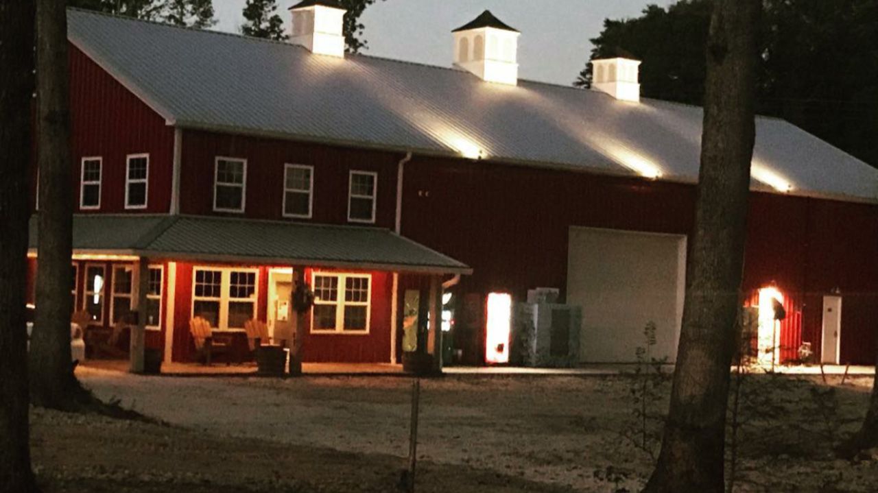 Red barn with white roof and cupolas, lit at night; trees in the foreground.