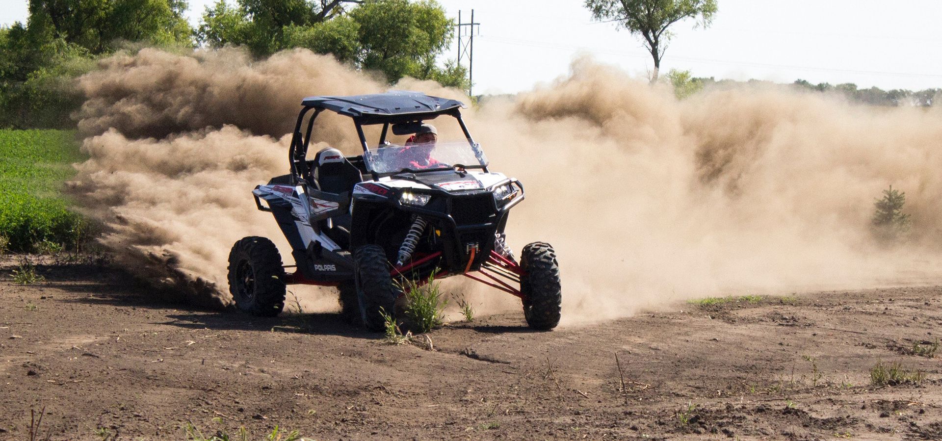 A UTV kicks up a large cloud of dust while driving on a dirt path.