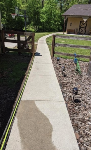 A concrete walkway leading to a house with a fence in the background.