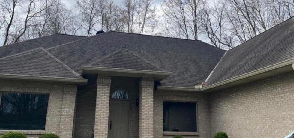 A large brick house with a gray roof and trees in the background.