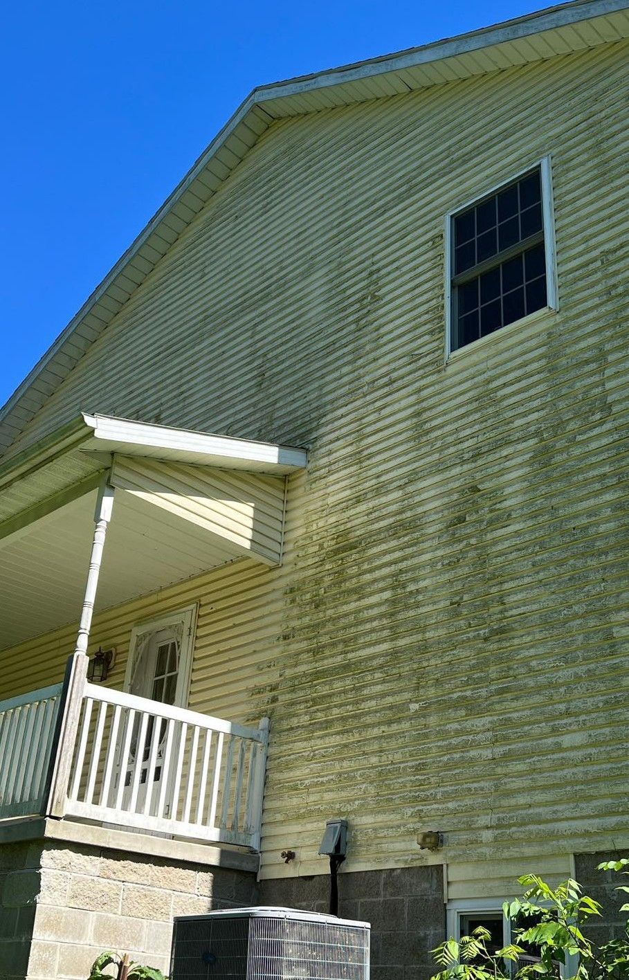 A yellow house with a white porch and a blue sky in the background.