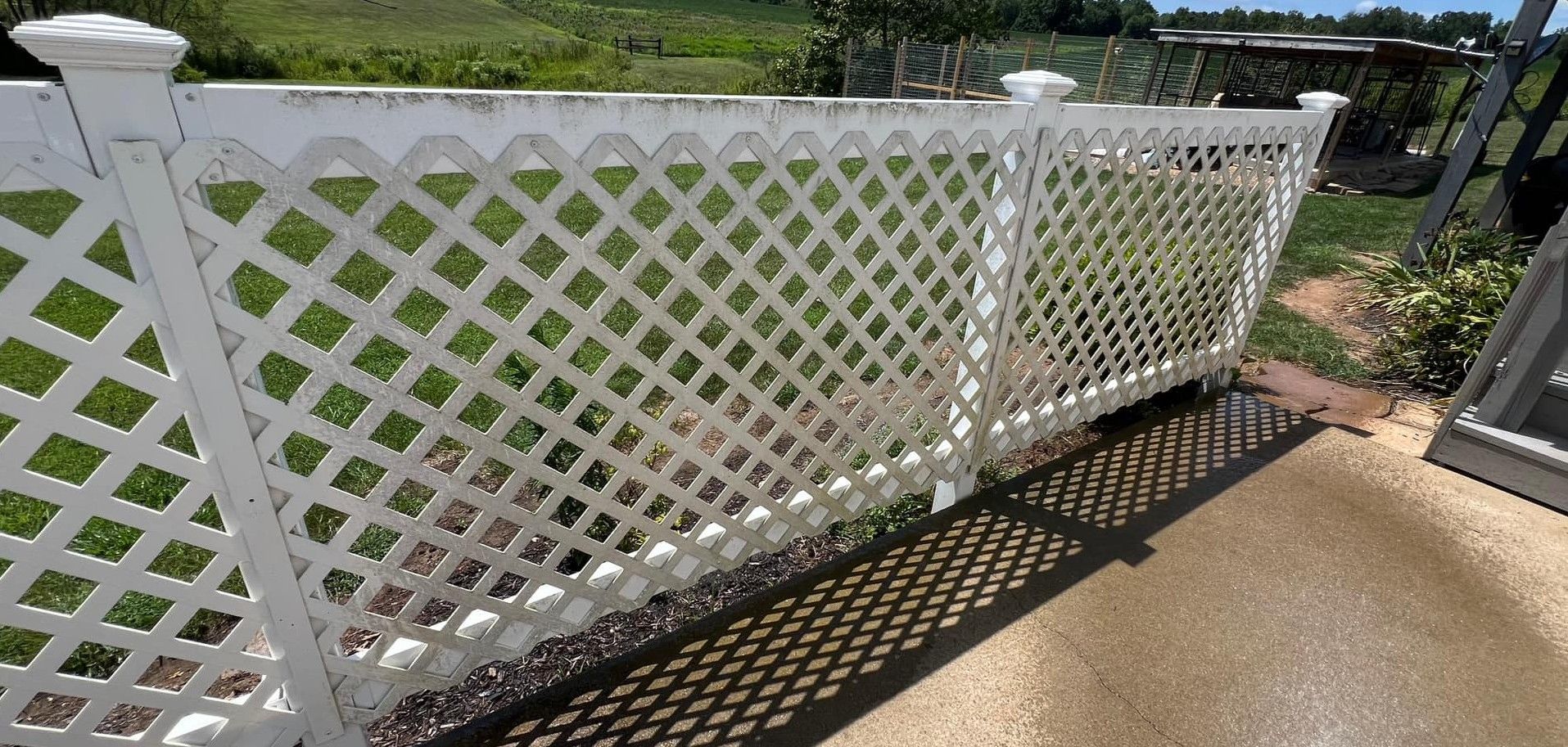 A white lattice fence is sitting on top of a concrete walkway.