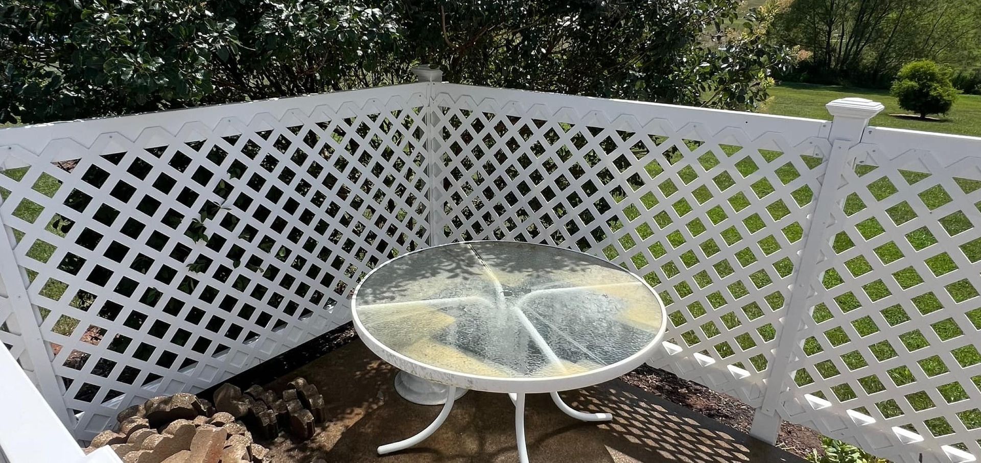 A table with a glass top is sitting in front of a white lattice fence.