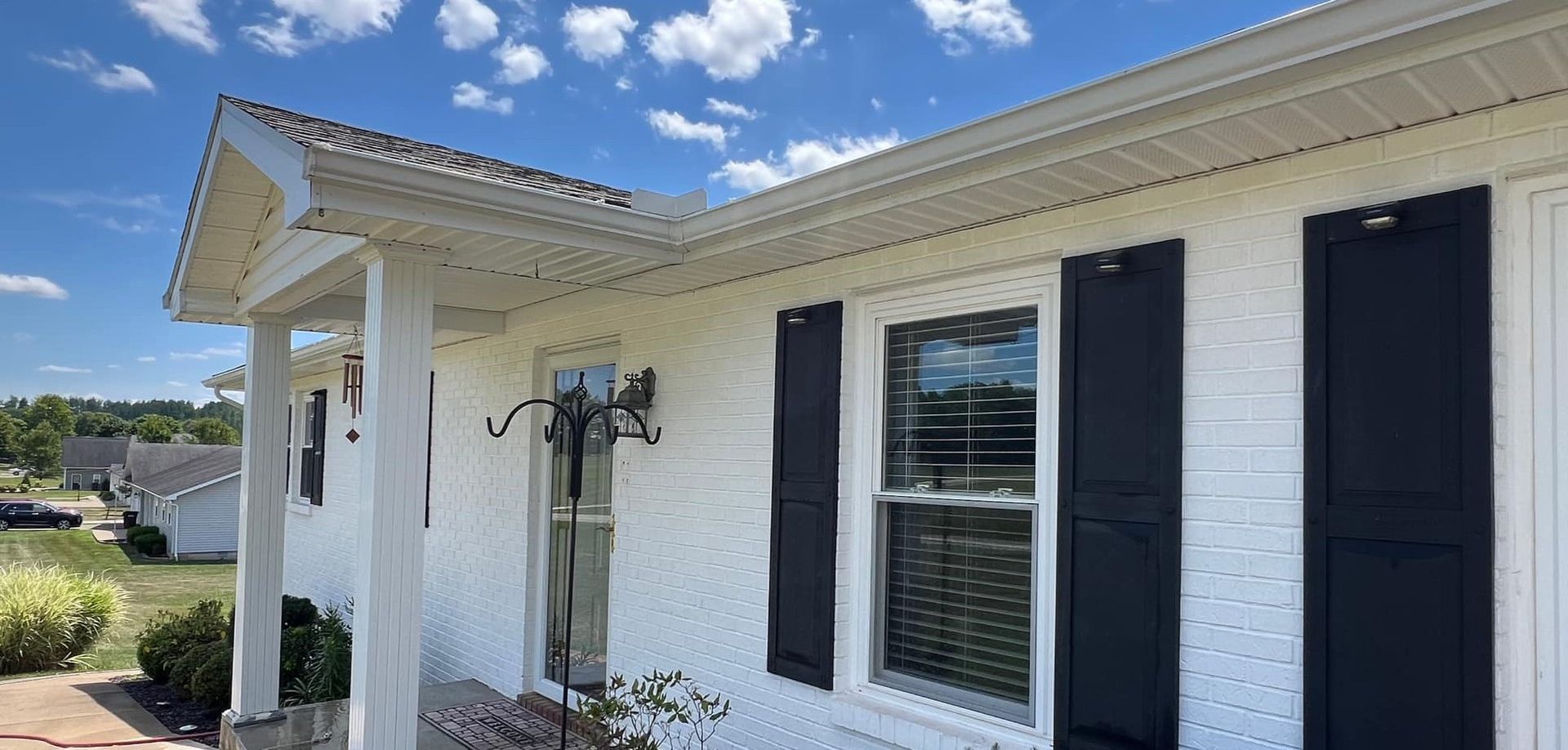 A white house with black shutters and a porch on a sunny day.
