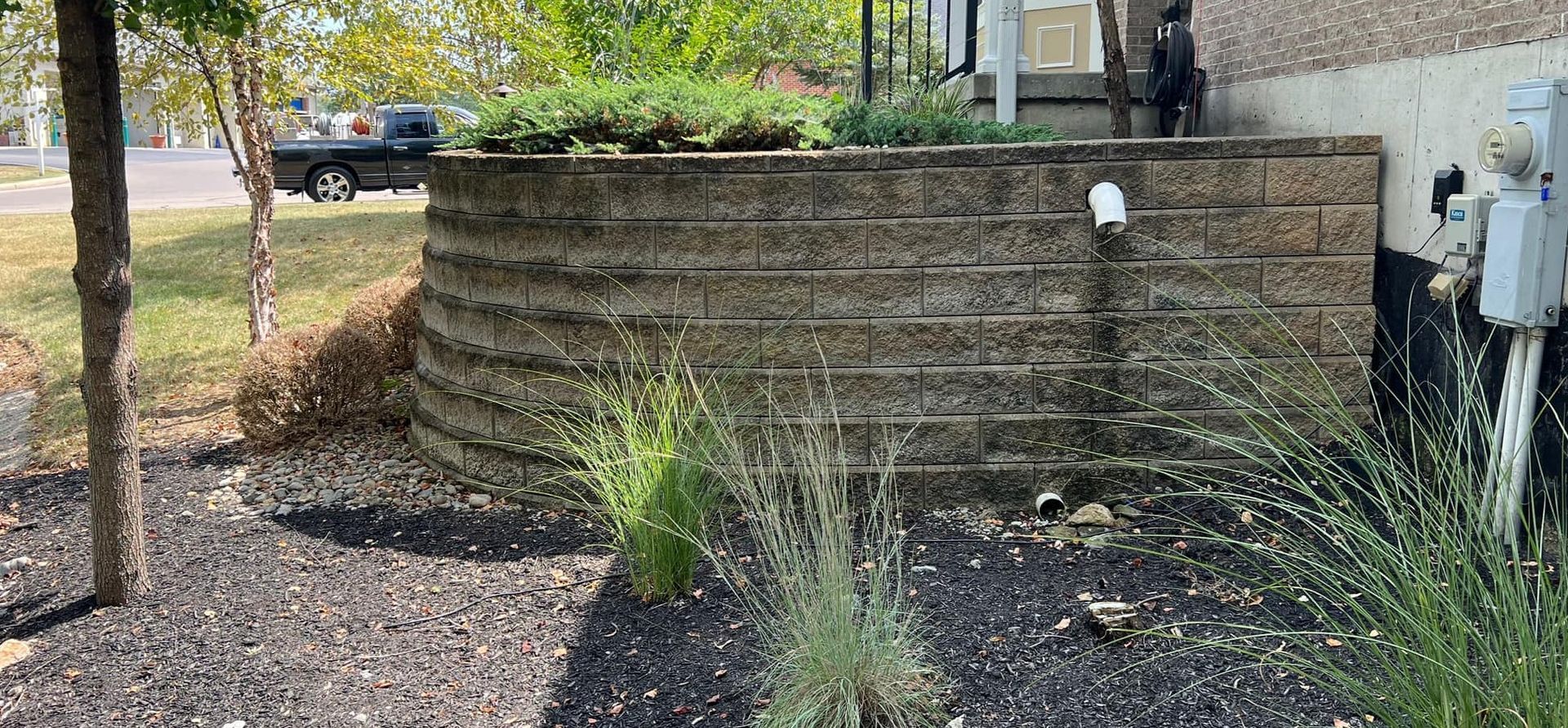 A brick wall is surrounded by mulch and trees in front of a house.