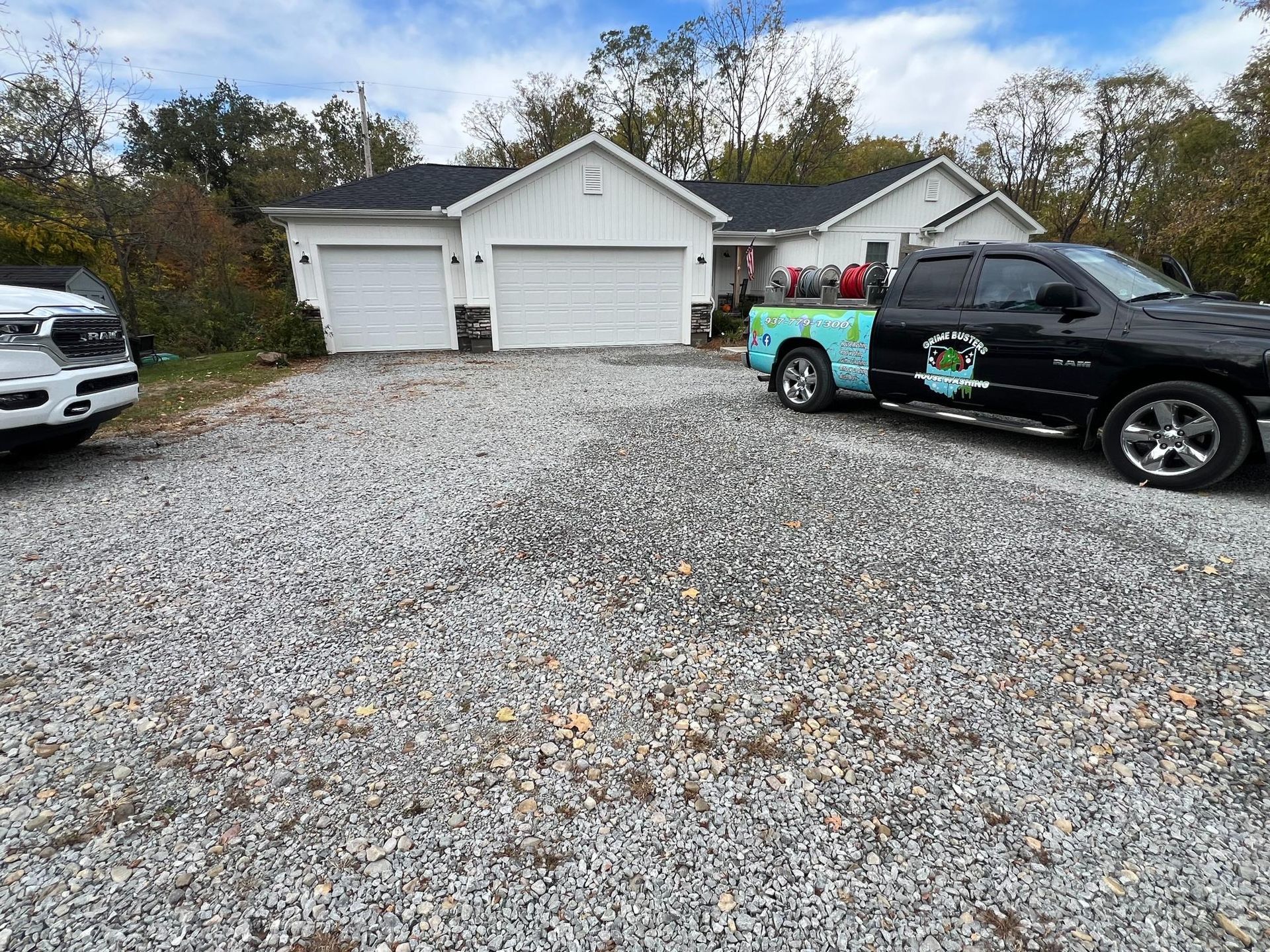 Gravel driveway with a white garage and two parked cars, including a black truck and a colorful wrapped car