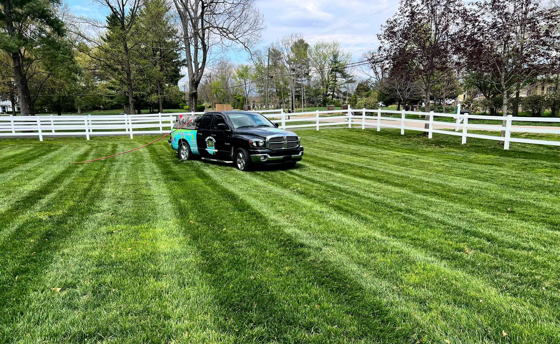 Black pickup truck on a green lawn beside a white fence on a sunny day