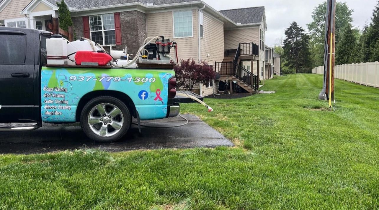 Decorated blue truck parked in a driveway beside a grassy yard and beige house