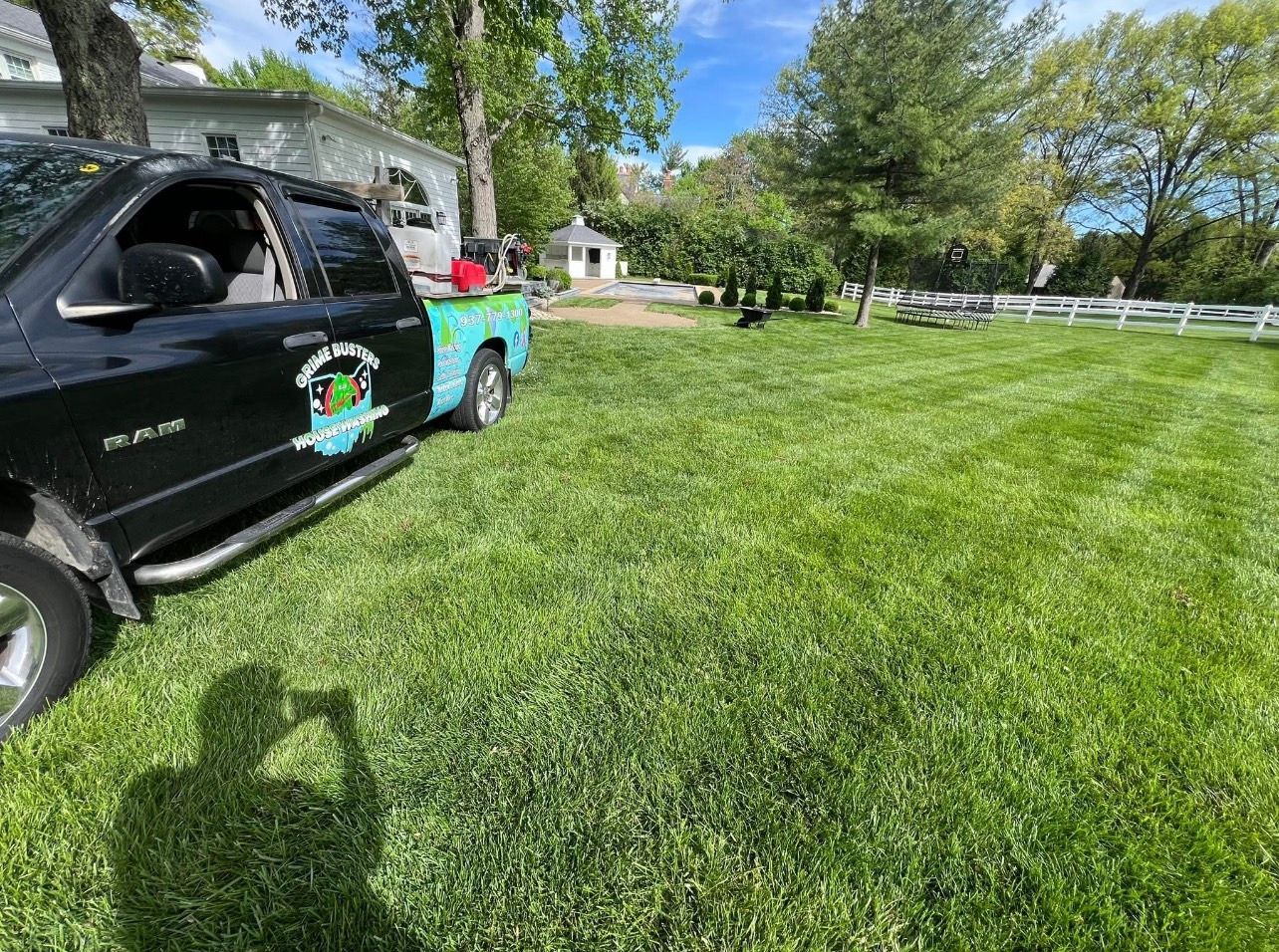 Black pickup truck parked on a grassy lawn beside a house, with trees and a bright blue sky.