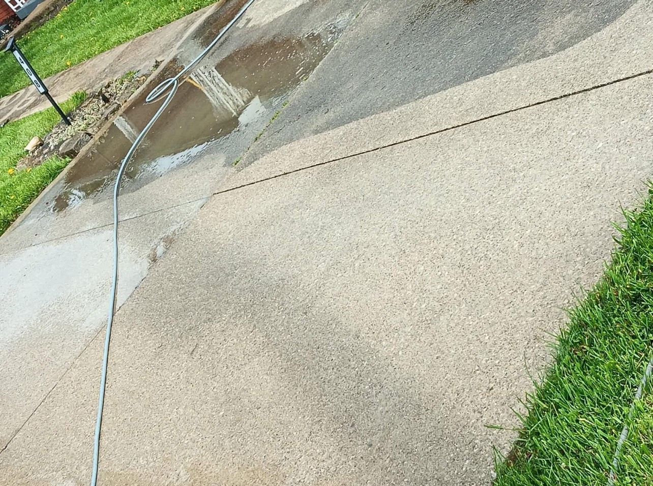 Wet sidewalk with puddles and a hose spraying water across the concrete path.