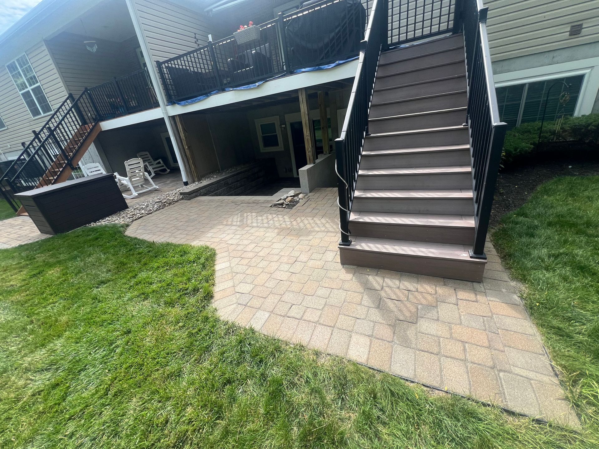 Apartment patio with brick pavers, grass, and an outdoor staircase to an upper deck.