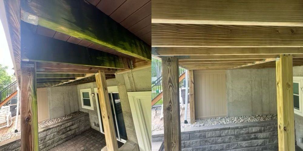Covered porch under a house with wooden beams, stairs, and a concrete foundation wall