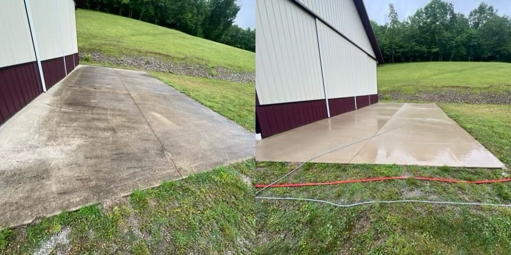 Concrete ramp beside a white barn with maroon trim, showing a grassy slope and paved walkway