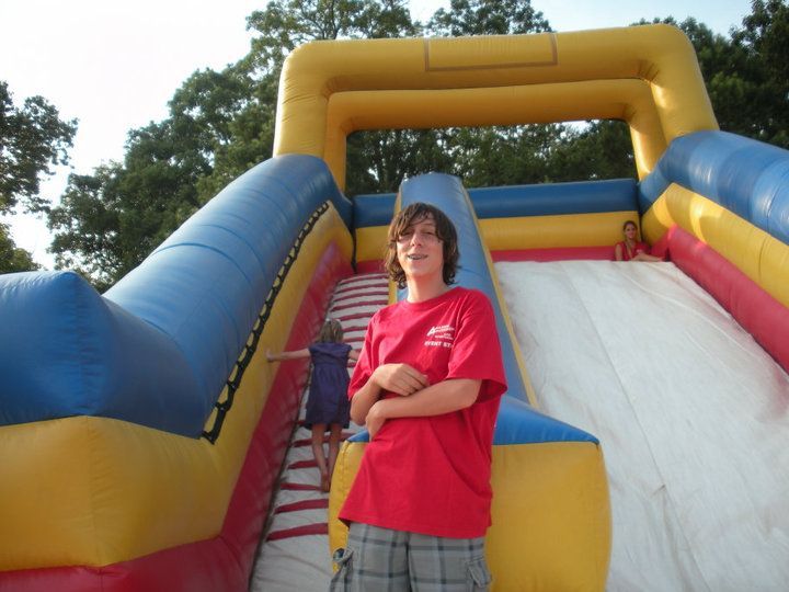 A person in a red shirt stands in front of a yellow, blue, and red inflatable slide.