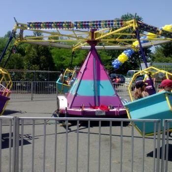 A colorful amusement park swing ride featuring a purple and blue conical base with hanging seats, set outdoors.