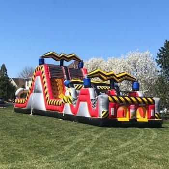 A red, white, and black inflatable obstacle course set up on a grassy lawn under a clear blue sky.