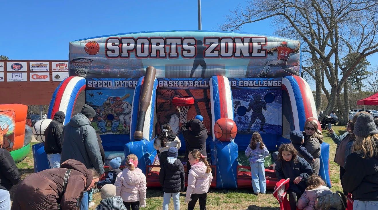 People gathered at a blue-and-red Sports Zone inflatable booth, with children and adults playing outdoors.