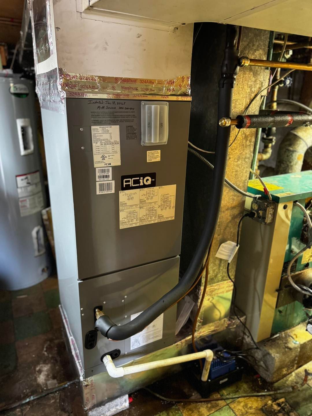 A grey HVAC air handler unit standing in a basement next to a water heater and a condensate pump.