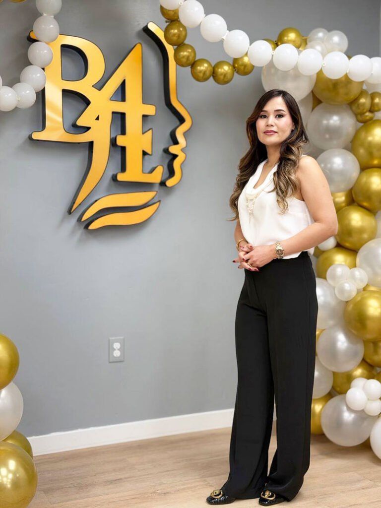 Woman standing beside a gold “B4” balloon wall with white, gold, and silver balloons on a gray backdrop