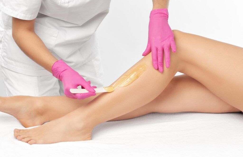 Gloved esthetician applying wax to a client's leg during hair removal treatment